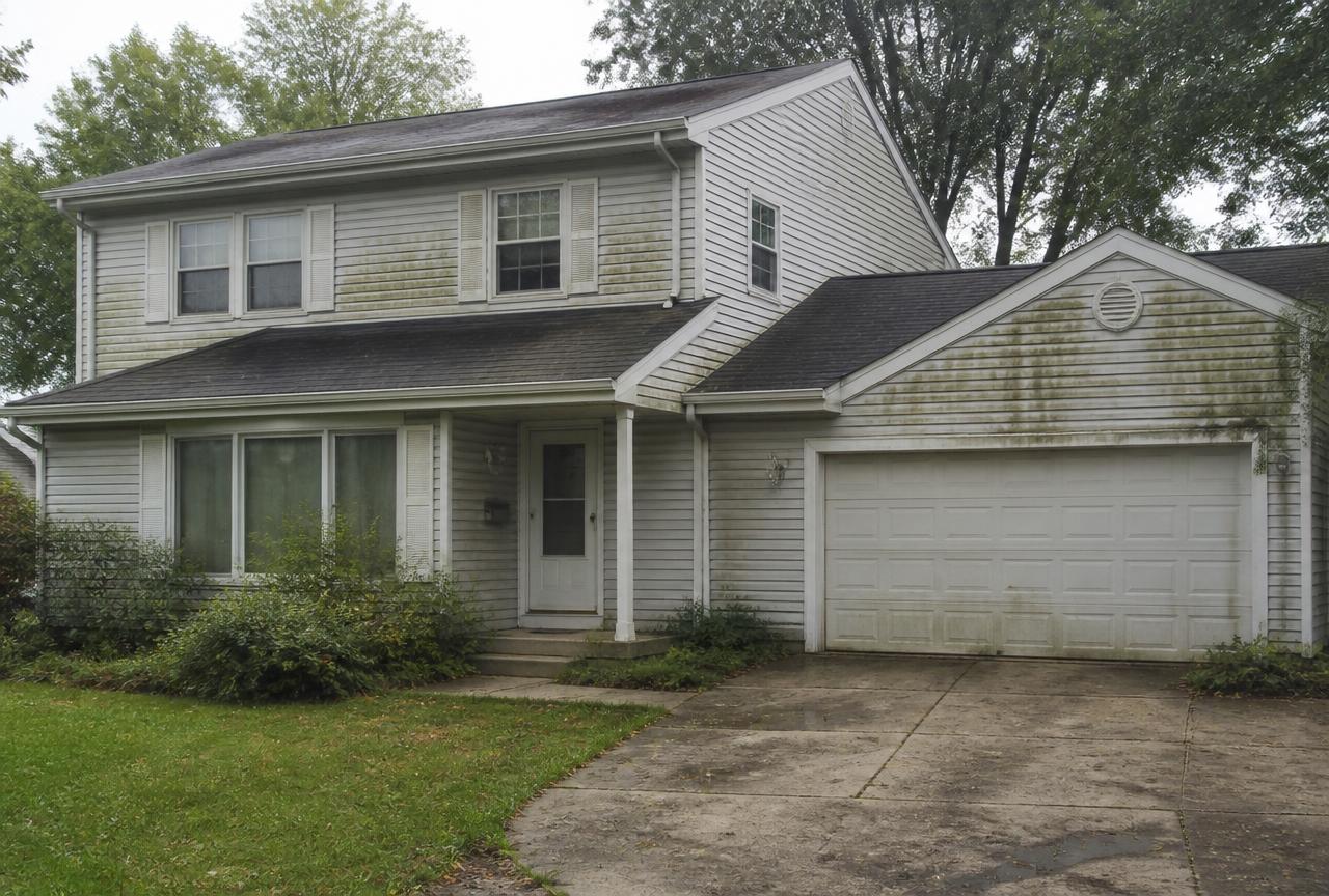 North Shore home with algae streaks on the siding, stained roof, and dirty concrete driveway before soft washing