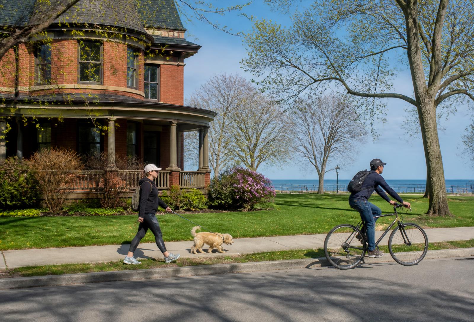 Evanston residents walking a dog and cycling past a brick Victorian home near the Lake Michigan shoreline